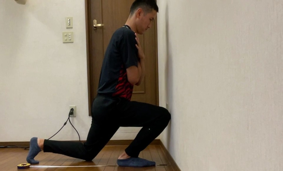 かかとを床につけたまま、膝を壁に近づけている様子